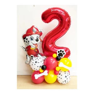 Könnte beinhalten: Eine festliche Ballonanordnung mit einem großen roten Ballon in Form der Zahl 2 und einem Marshall-Ballon von Paw Patrol. Die Anordnung umfasst rote, gelbe, schwarze und weiße Ballons, einige mit Pfotenabdrücken. Der Ballon mit der Zahl 2 trägt den Text "Tara is Two".