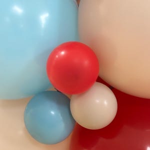 May include: Close-up of a cluster of colorful balloons in shades of red, white, light blue, and peach. The balloons are round and inflated, creating a festive and celebratory atmosphere. Perfect for a party or event.