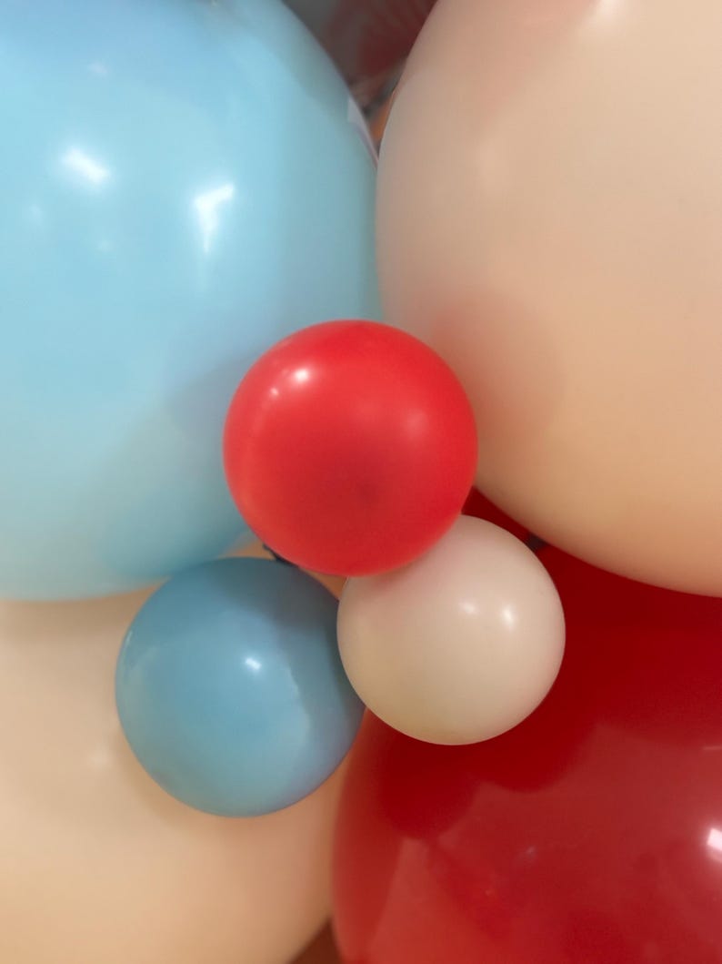 May include: Close-up of a cluster of colorful balloons in shades of red, white, light blue, and peach. The balloons are round and inflated, creating a festive and celebratory atmosphere. Perfect for a party or event.