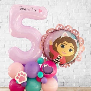 Könnte beinhalten: Ein rosa Ballon in Form der Zahl 5 mit dem Text "Tara is Five" und einem Herz. Das Ballonarrangement umfasst einen Charakterballon und kleinere Ballons in Rosa, Lila, Türkis und Magenta. Ein Pfotenabdruck-Ausschnitt ist ebenfalls enthalten.