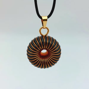 Könnte beinhalten: Eine Halskette mit einem Anhänger aus schwarzem und kupferfarbenem Drahtgeflecht an einer goldenen Kette.