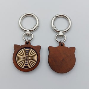 May include: Two wooden keychains with silver key rings. One keychain features a brown cat face with a gold spiral design. The other keychain features a plain brown cat face.
