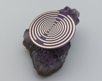 May include: A purple and gold circular sticker with a concentric circle design, placed on top of a cluster of amethyst crystals.