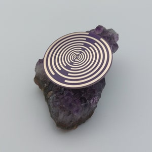 May include: A purple and gold circular sticker with a concentric circle design, placed on top of a cluster of amethyst crystals.