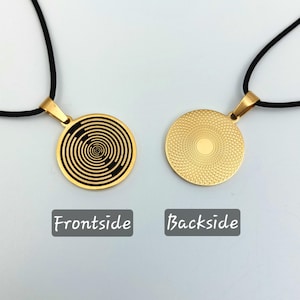 Könnte beinhalten: Eine goldene Halskette mit einem runden Anhänger, der auf der Vorderseite ein schwarz-weißes Spiralmuster und auf der Rückseite ein strukturiertes Golddesign aufweist.