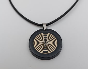Puede incluir: Un collar negro con un colgante redondo que presenta un diseño de círculo concéntrico dorado.