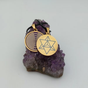 May include: Two gold pendants on a black cord, resting on a bed of purple amethyst crystals. One pendant features a geometric design, while the other has a swirling pattern.