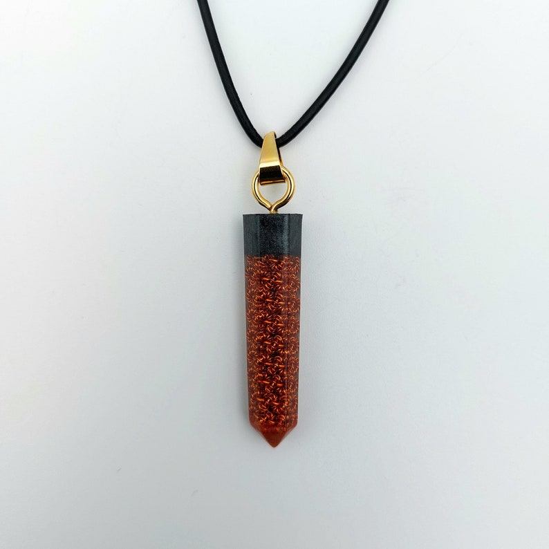 Puede incluir: Un collar con un colgante de resina negro y cobre. El colgante tiene forma de punta larga y fina.