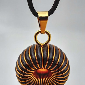 May include: A gold pendant necklace with a black and copper wire coil design. The pendant is shaped like a circle with a hole in the center.