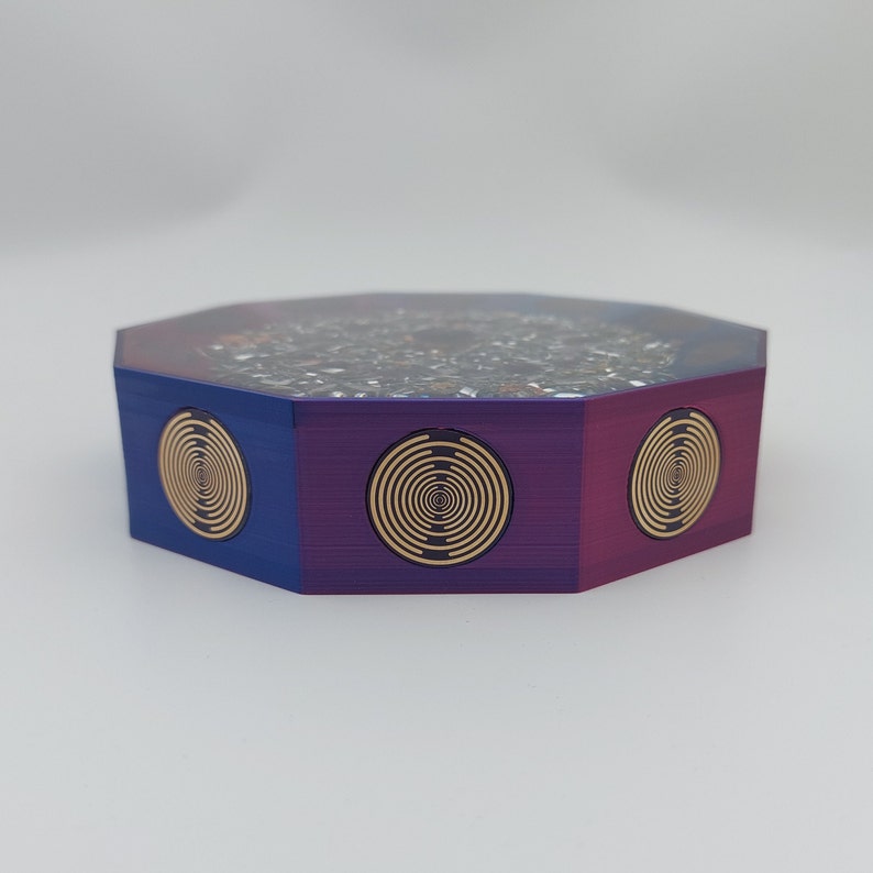 May include: Octagonal shaped box with a purple, blue, and red finish. The box has a black and white speckled top and three gold circular designs on the sides.