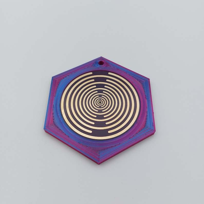 May include: A hexagonal pendant with a concentric circle design in gold on a dark purple background. The pendant has a blue and purple gradient finish.