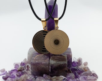 May include: Two gold-colored pendant necklaces with black cords. One pendant features a spiral design, the other a textured pattern. The pendants hang against a backdrop of amethyst crystals and a tall, purple crystal.