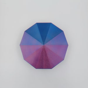 May include: A multi-faceted, octagonal-shaped object with a blue and purple iridescent finish. The object has a geometric design with a central point.