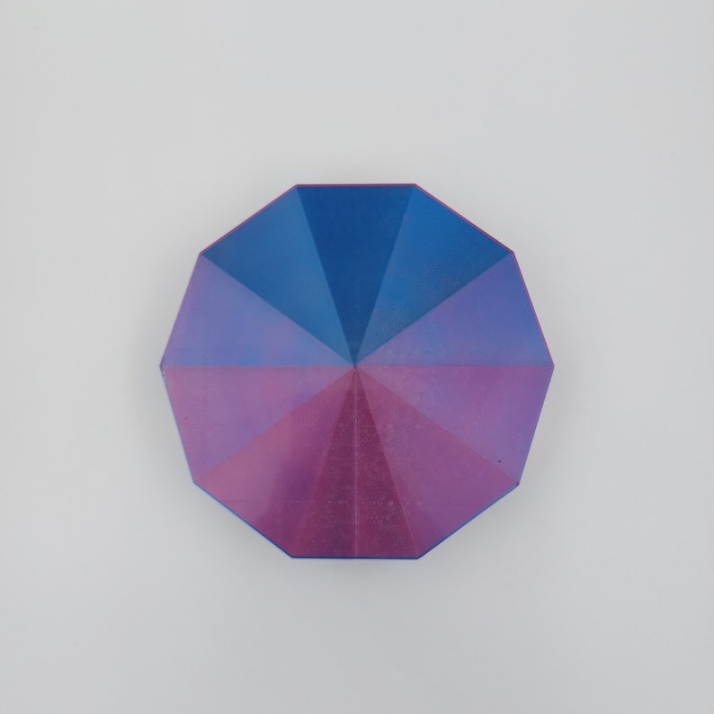 May include: A multi-faceted, octagonal-shaped object with a blue and purple iridescent finish. The object has a geometric design with a central point.