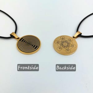 May include: A gold-colored pendant necklace with a black cord. The front of the pendant features a black and white spiral design. The back of the pendant features a geometric design.