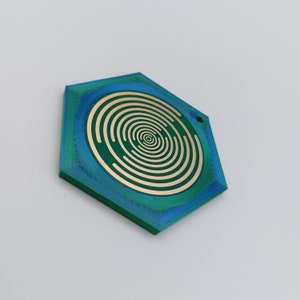 May include: A hexagonal, green and blue, plastic pendant with a concentric circle design in gold.