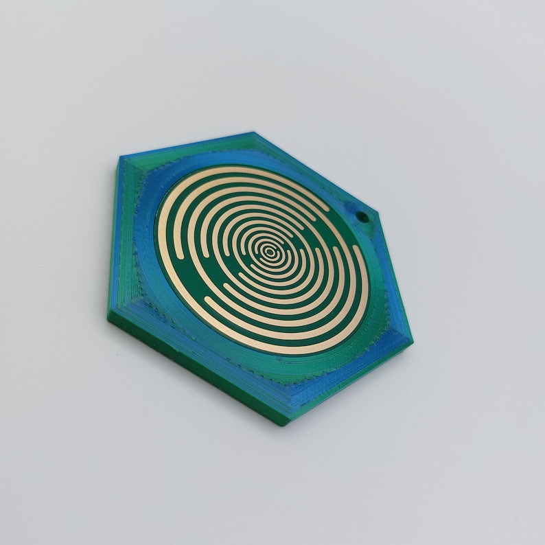 May include: A hexagonal, green and blue, plastic pendant with a concentric circle design in gold.