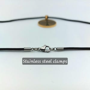 May include: A black cord necklace with stainless steel clamps. The necklace has a round pendant with a gold finish.
