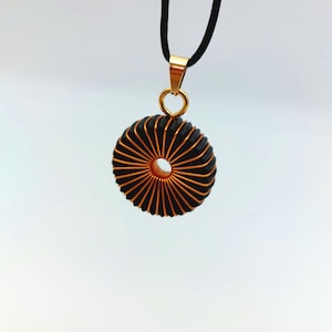 May include: A gold pendant necklace with a black and copper wire coil design. The coil is shaped like a circle with a hole in the center.