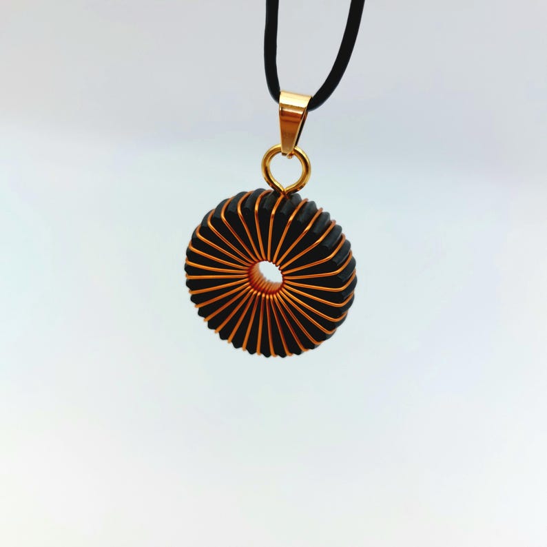 May include: A gold pendant necklace with a black and copper wire coil design. The coil is shaped like a circle with a hole in the center.