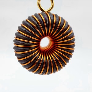 May include: A copper and black wire coil pendant with a gold loop at the top. The coil is wound in a spiral pattern and has a circular opening in the center.