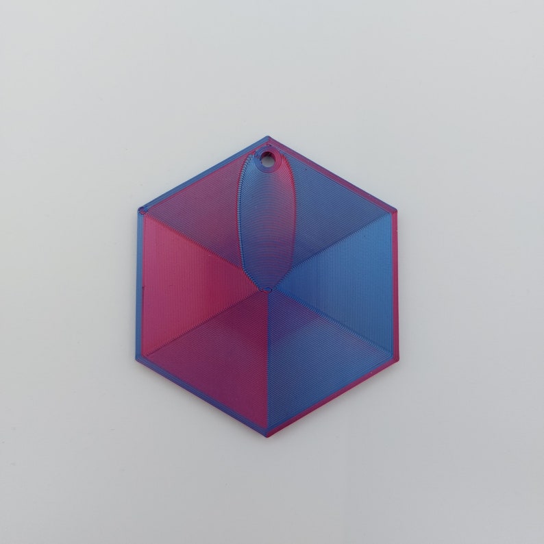 May include: A 3D printed hexagonal ornament with a blue and pink gradient. The ornament has a small hole at the top for hanging.