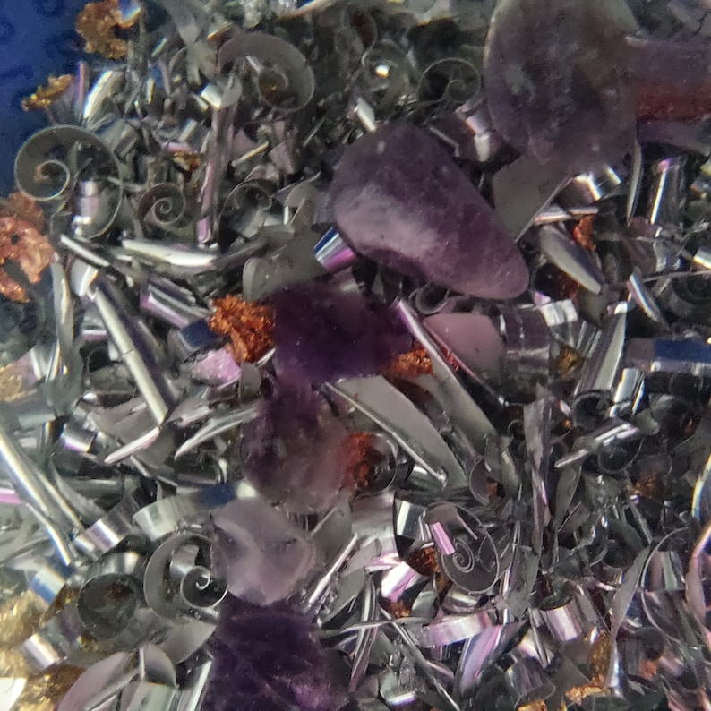 May include: A close-up of a mixture of metal shavings and purple amethyst crystals. The metal shavings are silver and have a shiny, reflective surface. The amethyst crystals are various sizes and shapes.