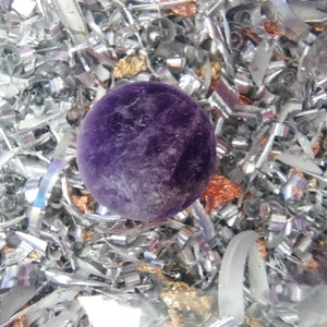 May include: A close-up of a purple amethyst sphere surrounded by silver and gold metallic confetti.
