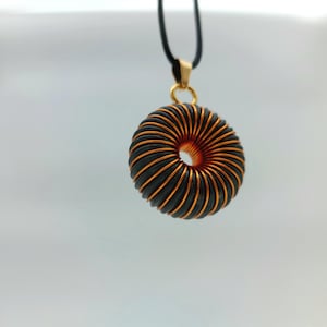 May include: A gold pendant necklace with a black and copper wire coil design. The coil is shaped like a donut.