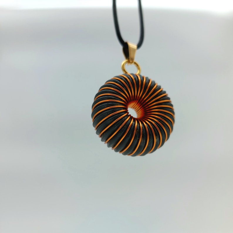 May include: A gold pendant necklace with a black and copper wire coil design. The coil is shaped like a donut.