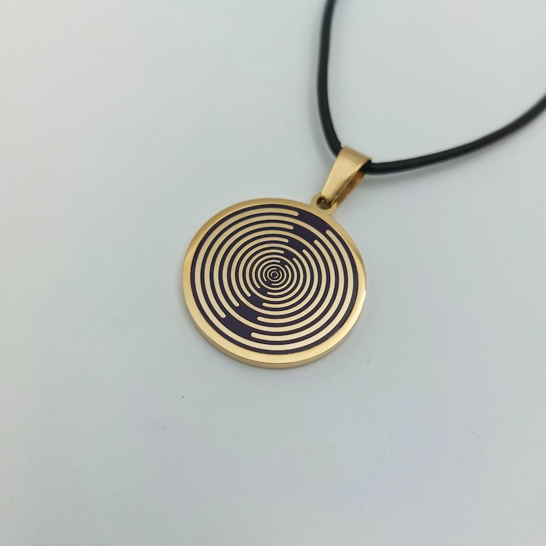 May include: A gold necklace with a round pendant featuring a black and gold spiral design.