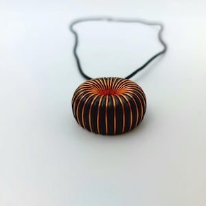 May include: A black cord necklace with a copper and black coil pendant. The coil is shaped like a donut.