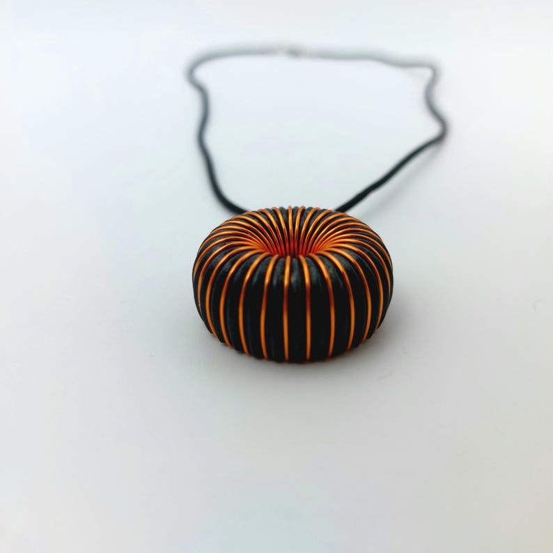 May include: A black cord necklace with a copper and black coil pendant. The coil is shaped like a donut.