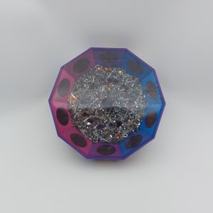 May include: A multi-faceted, octagonal, clear resin orb with a pink and blue swirl design. The orb is filled with small, metallic, silver, and copper pieces.