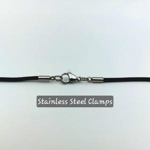 Puede incluir: Un collar de cord&oacute;n negro con abrazaderas de acero inoxidable. "Stainless Steel Clamps" est&aacute; escrito en negro debajo del collar.