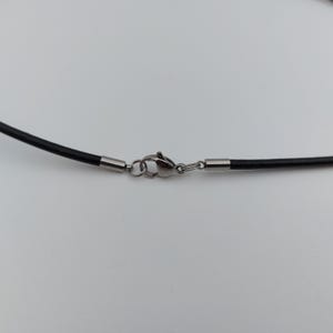 May include: Close-up of a black necklace cord with a silver-colored clasp. The cord is smooth and appears to be made of a flexible material. The clasp is a lobster claw style, with a small ring to attach to the other end of the necklace.