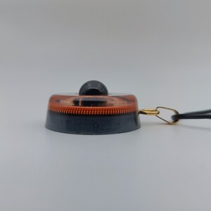 May include: A black and copper-colored light switch with a small black knob on top. The switch has a copper-colored ring around the middle and a black base. A gold-colored ring and black cord are attached to the side.