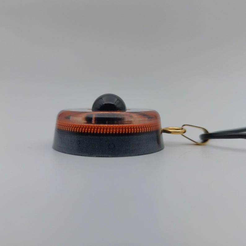 May include: A black and copper-colored light switch with a small black knob on top. The switch has a copper-colored ring around the middle and a black base. A gold-colored ring and black cord are attached to the side.