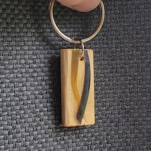 May include: A wooden keychain with a silver key ring. The wood is light brown with a dark blue and gold stripe running through it.