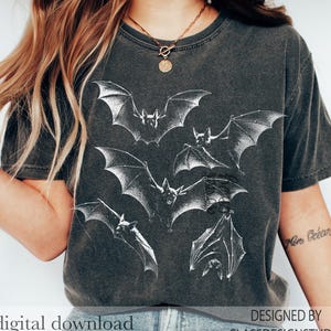 May include: A charcoal gray short-sleeve t-shirt featuring a white graphic print of multiple bats in flight and hanging positions. The shirt has a crew neckline and a vintage-style washed finish. The text digital download and designed by classdesignstudio is visible.