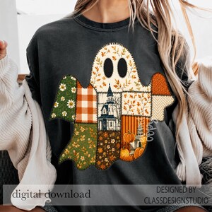 May include: A charcoal gray crewneck sweatshirt featuring a large ghost-shaped graphic composed of various patchwork patterns including autumn leaves, orange plaid, green floral prints, a haunted house, and pumpkins.