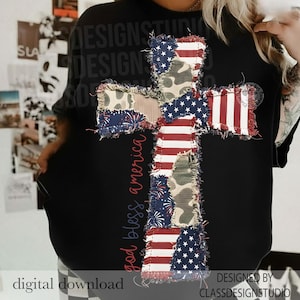 May include: Black crew neck t-shirt featuring a large cross design made of patchwork fabric. The cross incorporates elements of the American flag, camouflage, and fireworks patterns. The words "god bless america" are printed vertically on the left side.