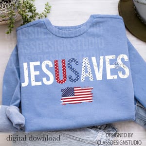 May include: A light blue sweatshirt with the words "JESUS SAVES" in distressed white lettering. The letter "U" in "JESUS" is filled with red stars, and the letter "S" in "SAVES" is filled with blue stars. An American flag graphic is below.