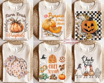 May include: Six cream-colored t-shirts featuring autumn-themed graphics. Designs include pumpkins, a jack-o'-lantern on a checkered background, a floral pumpkin, a cozy season collage with a ghost and cat, and chickens with the text Chick or Treat.