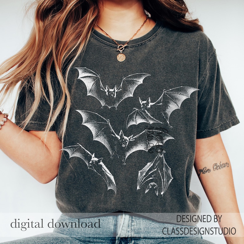 May include: A charcoal gray short-sleeve t-shirt featuring a white graphic print of multiple bats in flight and hanging positions. The shirt has a crew neckline and a vintage-style washed finish. The text digital download and designed by classdesignstudio is visible.