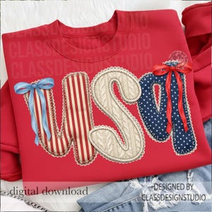 Puede incluir: Sudadera roja con la palabra "USA" en un dise&ntilde;o patri&oacute;tico. La "U" tiene un lazo azul, la "S" es un patr&oacute;n de punto de cable y la "A" es azul con estrellas blancas y un lazo rojo. La sudadera est&aacute; sobre un fondo de mezclilla.