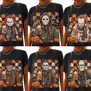 May include: A black t-shirt featuring a graphic print of six horror movie characters, each holding a pumpkin-themed coffee cup and wearing a plaid scarf. The background includes orange and black checkered patterns and autumn leaves.
