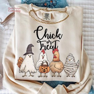 May include: Cream-colored sweatshirt with the text "Chick or Treat" and a graphic of four chickens in Halloween costumes. The chickens are wearing a witch hat, holding a pumpkin, and wrapped in bandages.