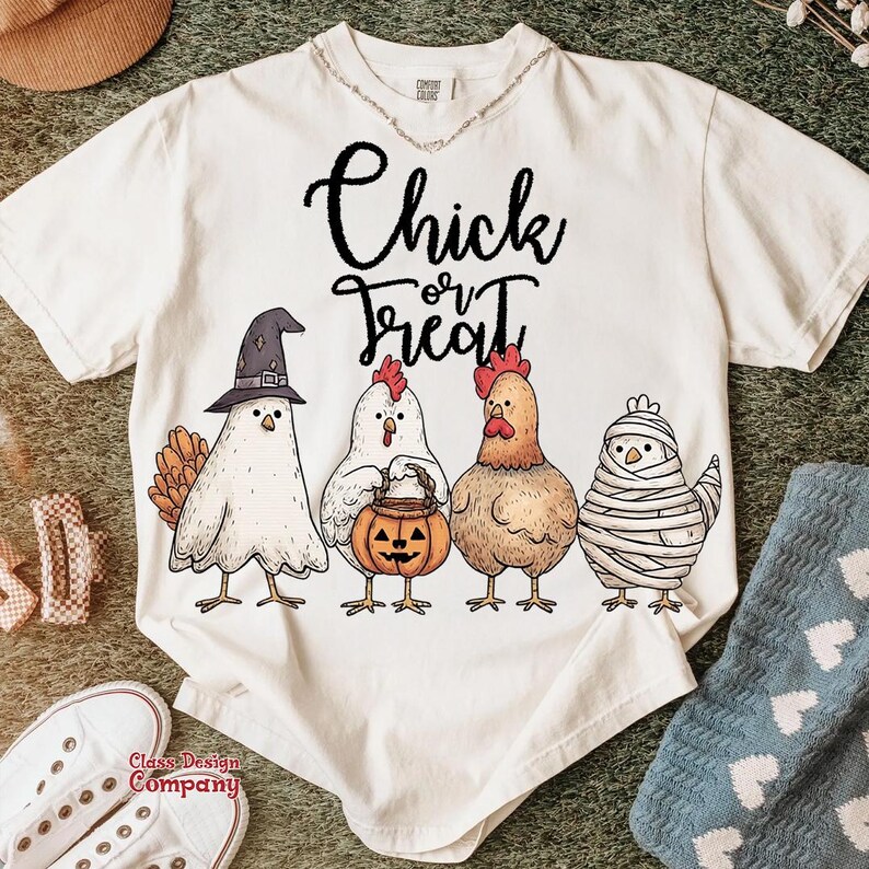 May include: Cream-colored t-shirt with the words "Chick or Treat" in black script. The shirt features four cartoon chickens dressed in Halloween costumes: a witch, a chicken holding a pumpkin, a chicken, and a mummy chicken.