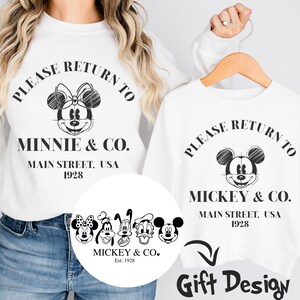 K&ouml;nnte beinhalten: Wei&szlig;es T-Shirt mit einer Schwarzwei&szlig;-Skizze von Minnie Maus und dem Text "Please Return to Minnie & Co. Main Street, USA 1928". Ein kleinerer Kreis darunter zeigt Mickey Mouse, Pluto, Goofy, Donald Duck und Daisy Duck mit dem Text "Mickey & Co. Est. 1928".